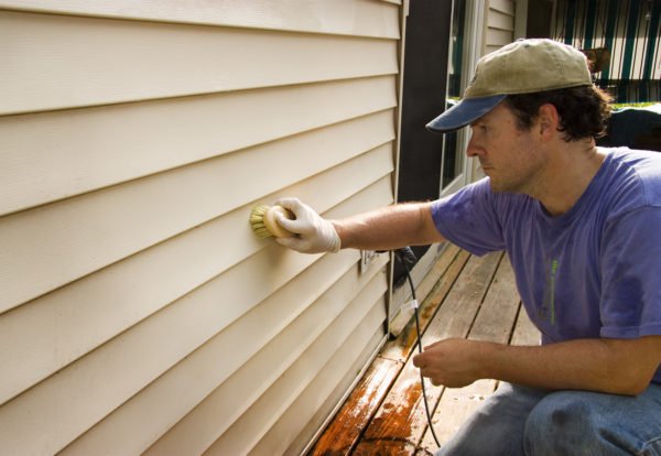 man cleaning beige vinyl siding with scrub brush