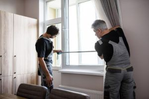 Two men measure a window. 