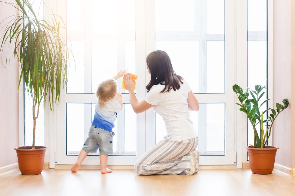 mother showing toddler how to clean window