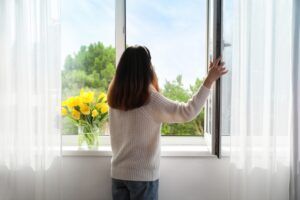 A woman looking out the window and thinking about X things to do to maintain her newly installed windows.